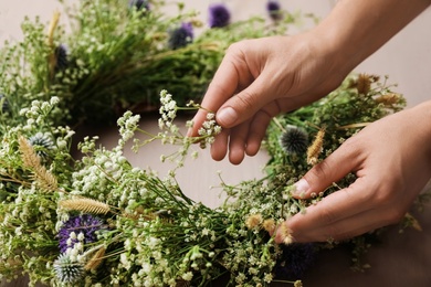 Woman making beautiful wreath of wildflowers at wooden table, closeup