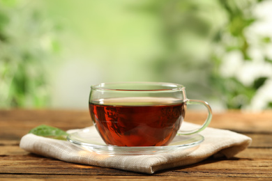 Cup of black tea on wooden table against blurred background. Space for text