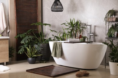 Photo of Modern white tub and beautiful green houseplants in bathroom. Interior design