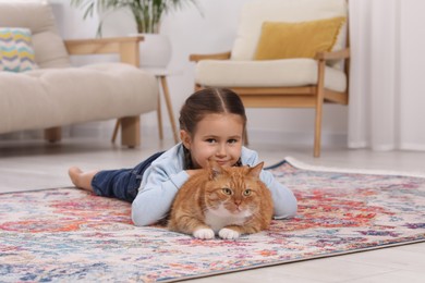 Smiling little girl and cute ginger cat on carpet at home