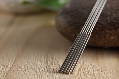 Photo of Acupuncture needles and spa stone on wooden table, closeup. Space for text