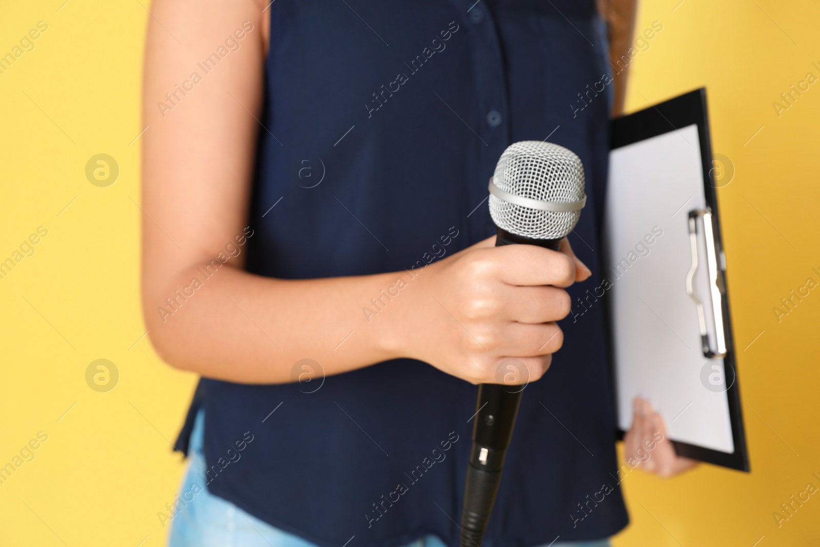 Photo of Young woman with microphone and clipboard on color background, closeup view