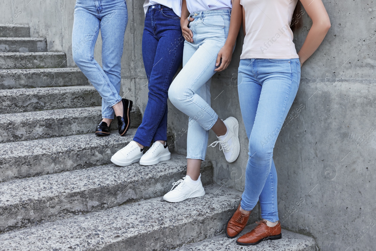 Photo of Women in stylish jeans on stairs near stone wall outdoors, closeup