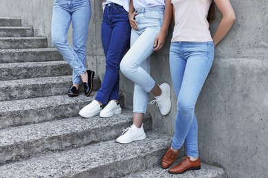 Women in stylish jeans on stairs near stone wall outdoors, closeup