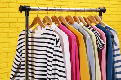 Rack with different stylish clothes near yellow brick wall