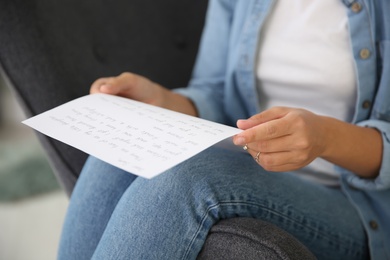 Photo of Young woman reading paper letter at home, closeup