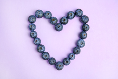 Heart of fresh ripe blueberries on lilac background, flat lay