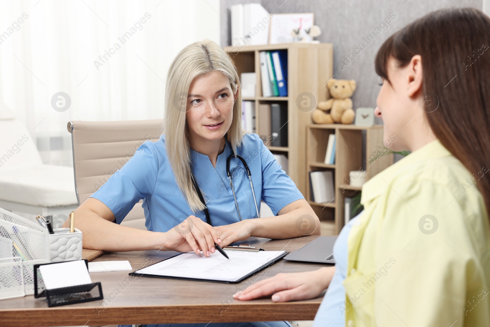 Photo of Doctor consulting pregnant patient at table in clinic