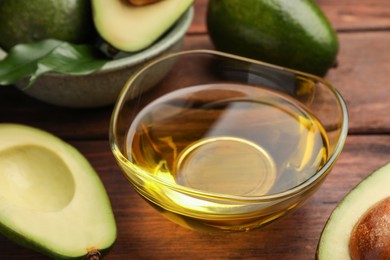 Photo of Cooking oil in bowl and fresh avocados on wooden table, closeup