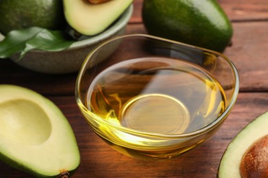 Cooking oil in bowl and fresh avocados on wooden table, closeup