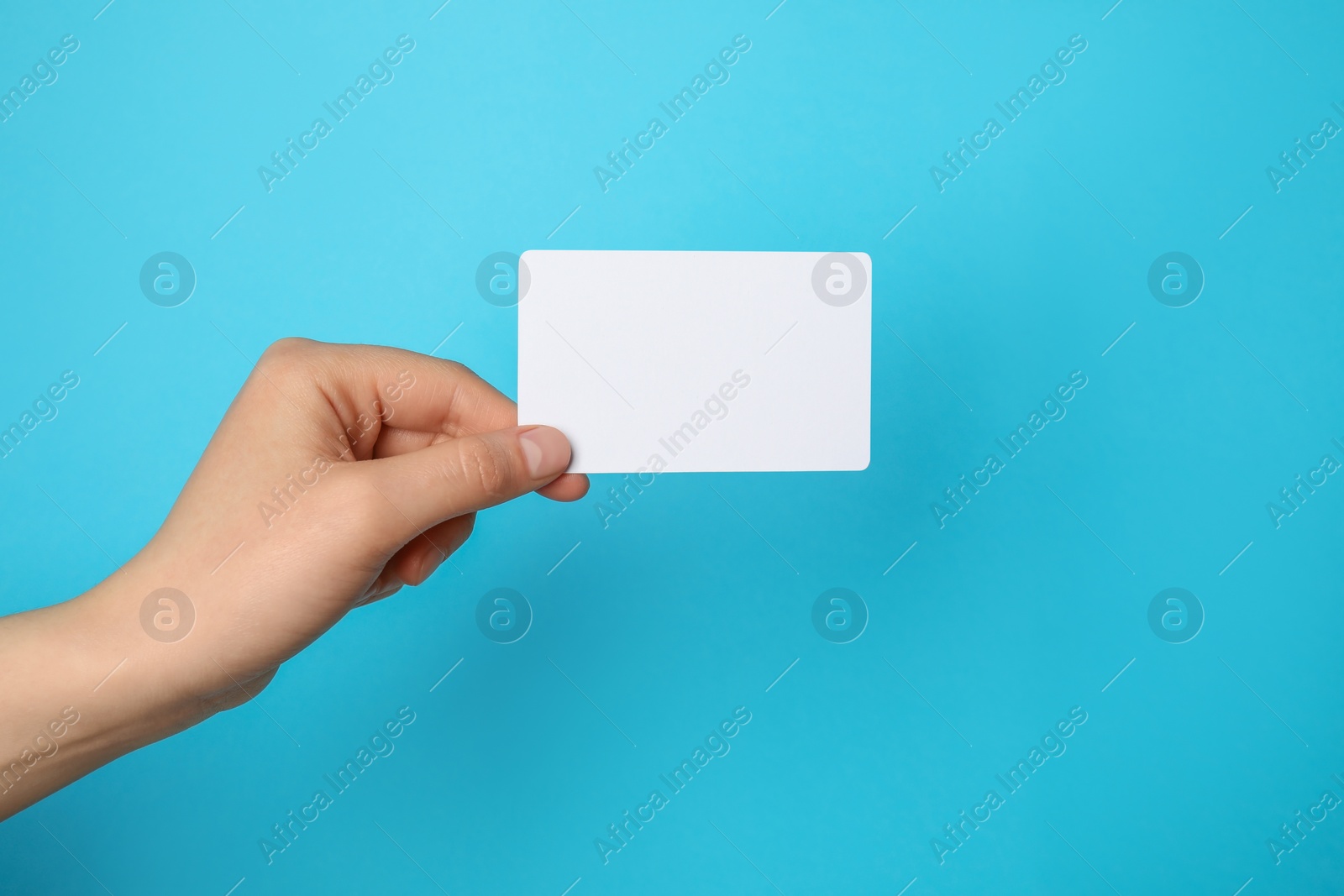 Photo of Woman holding blank gift card on light blue background, closeup