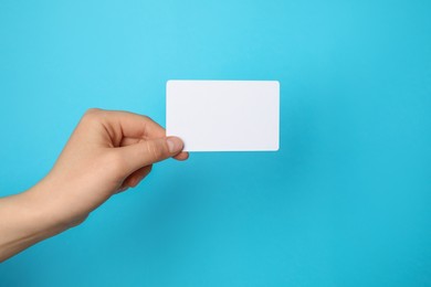 Photo of Woman holding blank gift card on light blue background, closeup