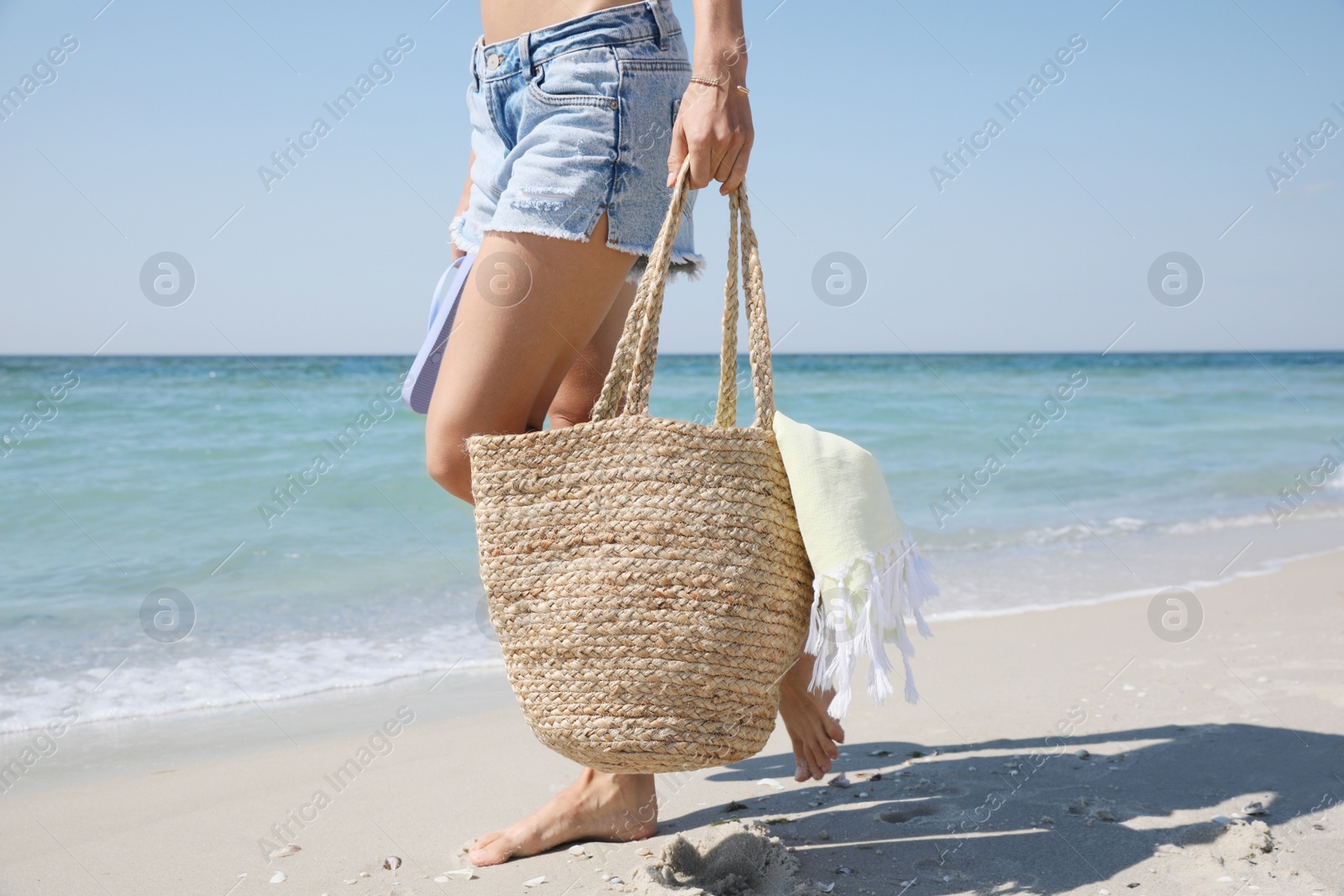 Photo of Woman with beach bag and flip flops walking near sea, closeup