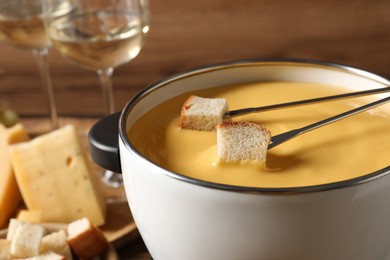 Pot of tasty cheese fondue and forks with bread pieces, closeup