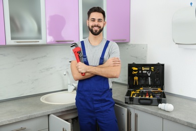 Photo of Male plumber with pipe wrench in kitchen. Repair service