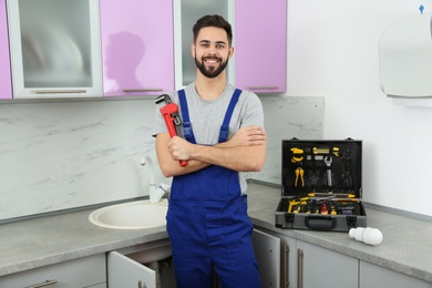 Male plumber with pipe wrench in kitchen. Repair service