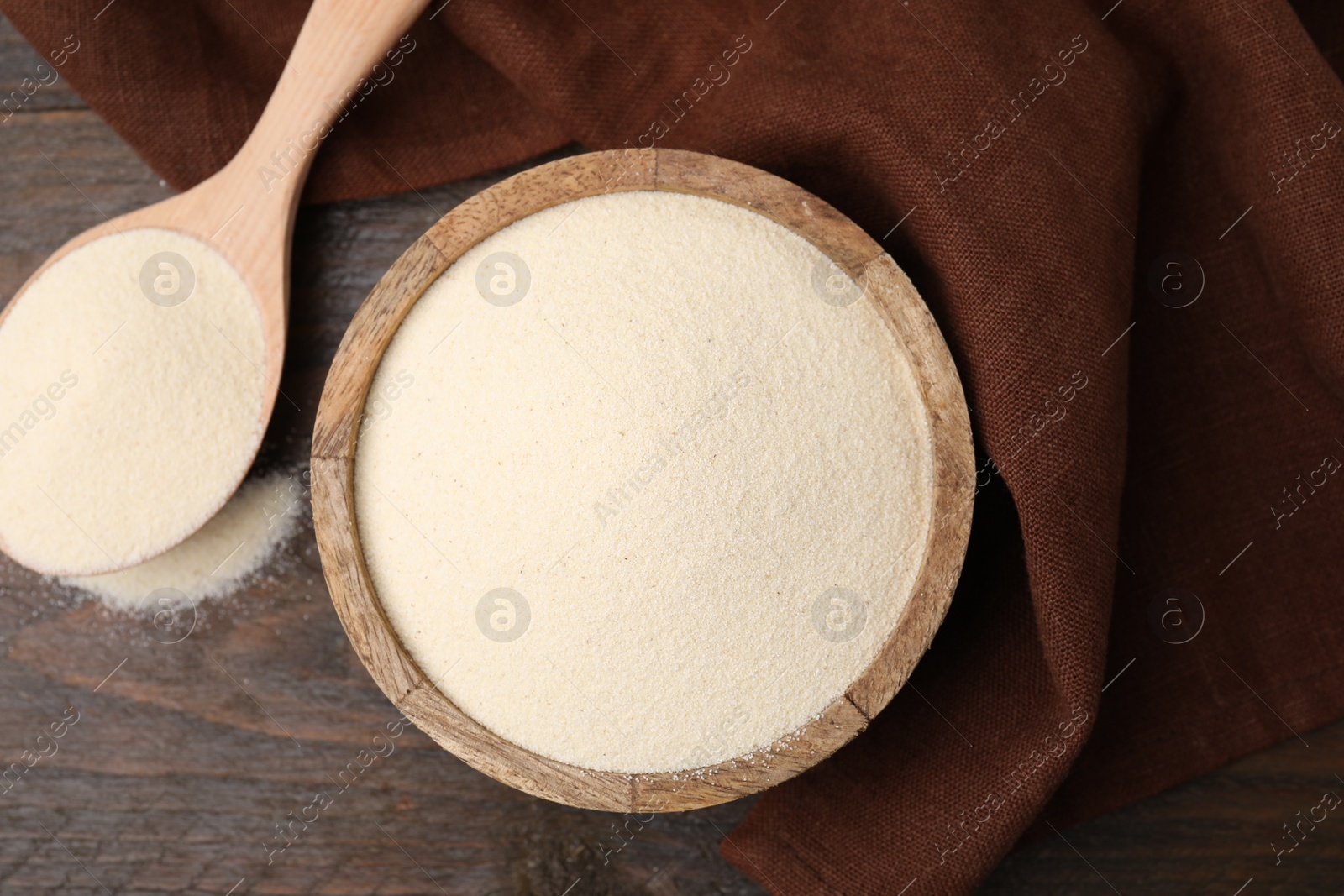 Photo of Uncooked organic semolina in bowl and spoon on wooden table, top view