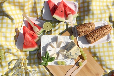 Photo of Delicious cheeses, fruits and bread on picnic blanket, flat lay