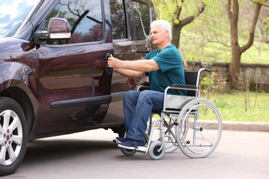 Mature man in wheelchair opening door of his van outdoors