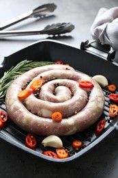 Photo of Pan with raw homemade sausage, chili pepper, garlic and rosemary on grey table, closeup