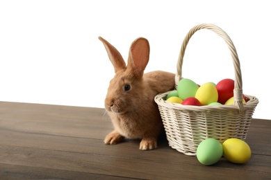 Cute bunny and basket with Easter eggs on wooden table against white background. Space for text
