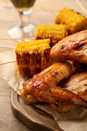 Photo of Delicious baked chicken wings and grilled corn served on wooden table, closeup