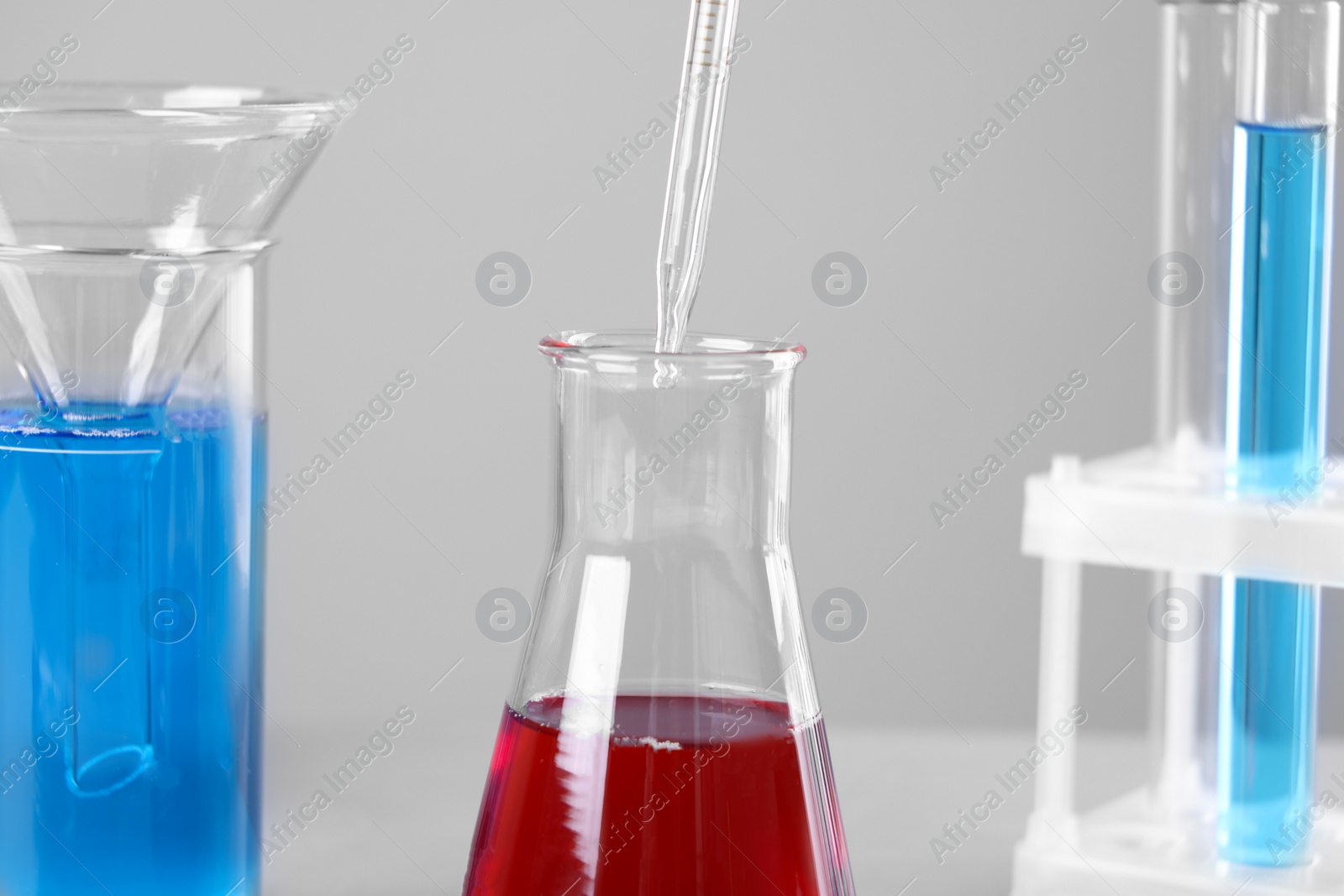 Photo of Dripping liquid from pipette into flask on grey background, closeup