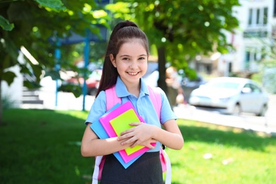 Cute little girl in school uniform with backpack and stationery on street