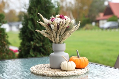 Beautiful bouquet of dry flowers and small pumpkins on glass table outdoors