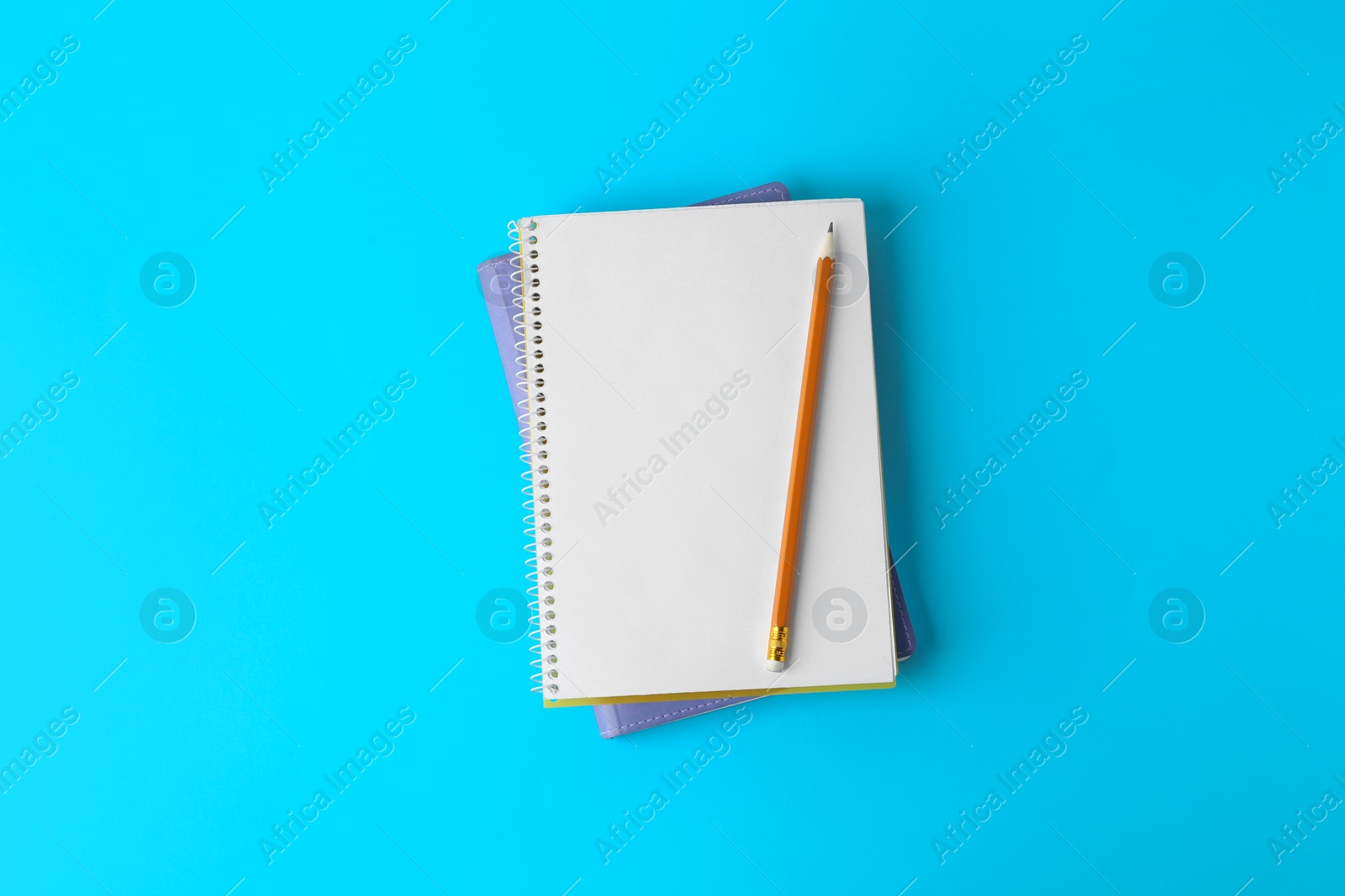 Photo of Notebooks with pencil on light blue background, top view