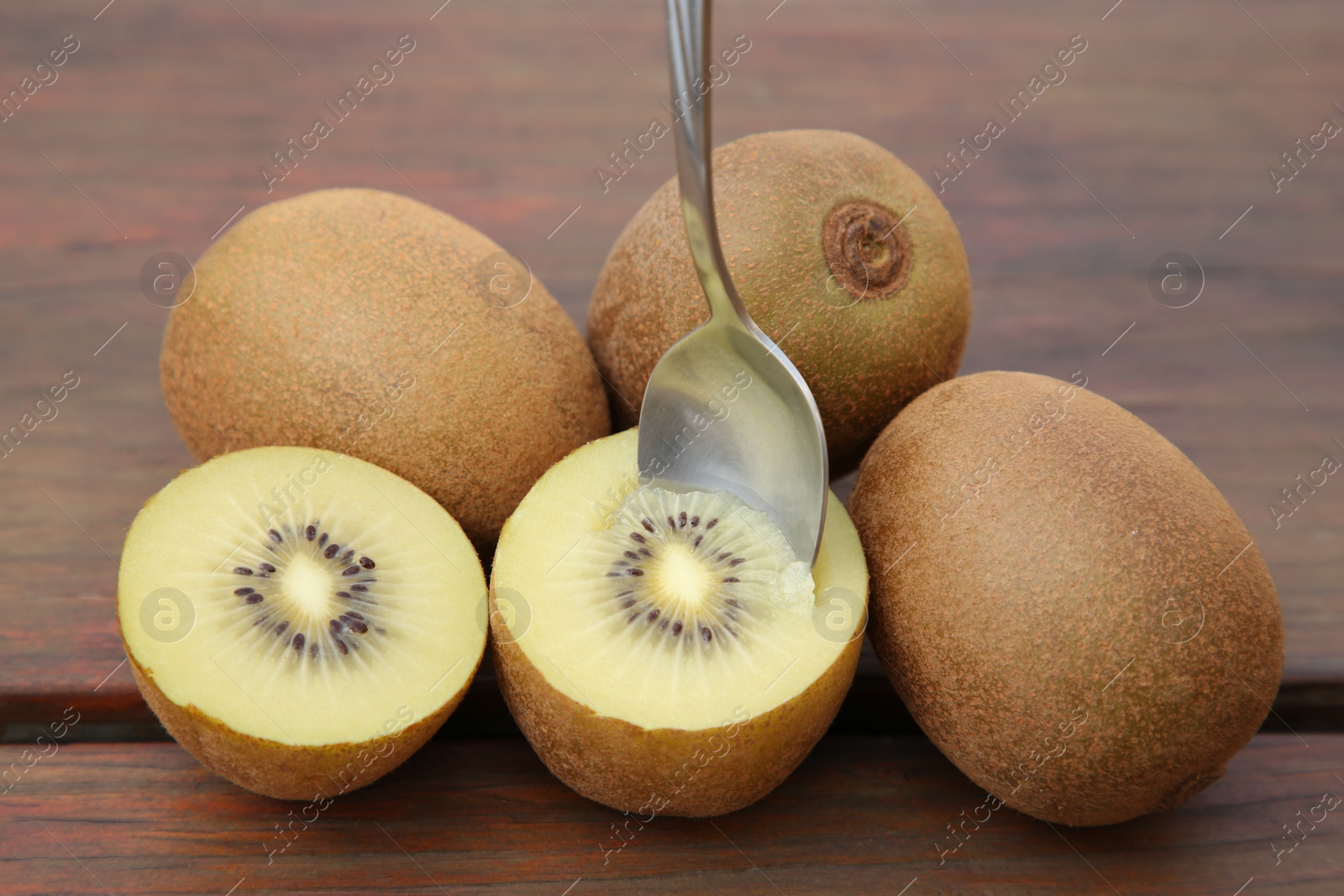 Photo of Fresh ripe yellow kiwis with spoon on wooden table