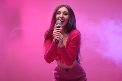 Beautiful woman with microphone singing on pink background