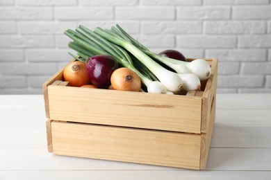 Crate with different kinds of onions on white wooden table