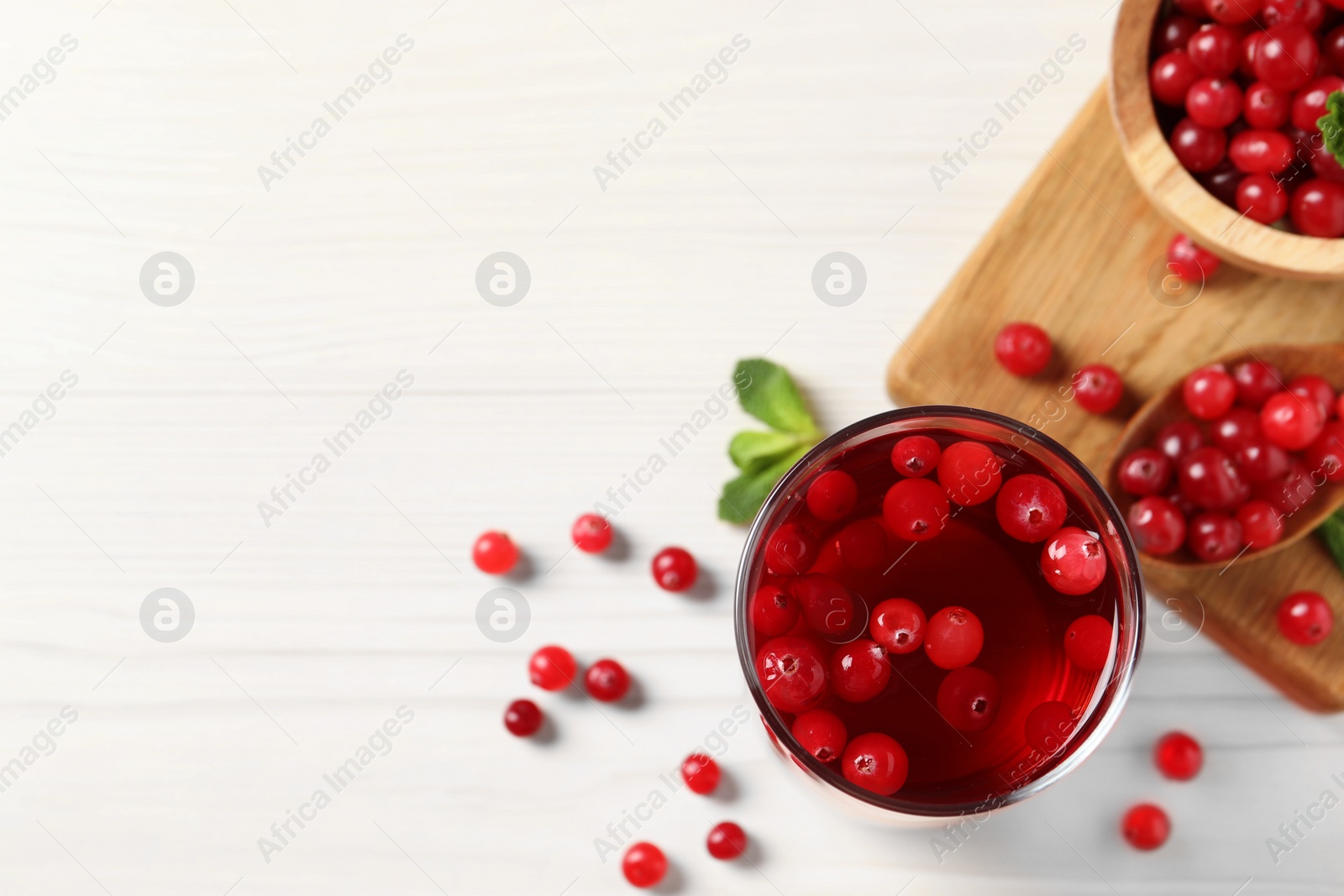 Photo of Tasty cranberry juice in glasses and fresh berries on white wooden table, flat lay. Space for text