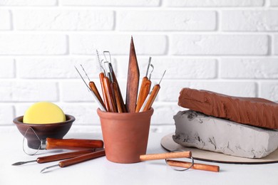 Clay and set of crafting tools on white textured table against brick wall