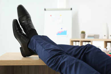 Photo of Lazy office employee resting with feet up on desk at workplace, closeup