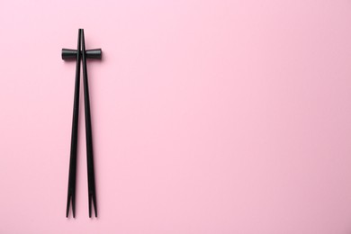 Photo of Pair of black chopsticks with rest on pink background, top view. Space for text
