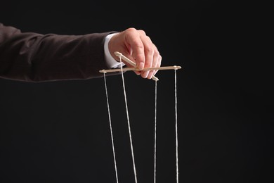 Photo of Man pulling strings of puppet on black background, closeup