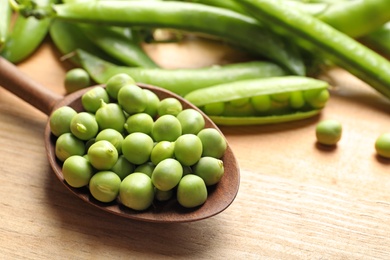 Photo of Spoon with green peas on wooden table, closeup