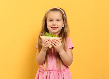 Cute little girl with tasty sandwich on yellow background