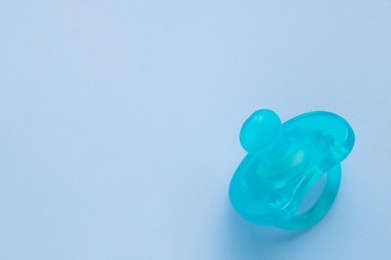One new baby pacifier on light blue background, top view. Space for text