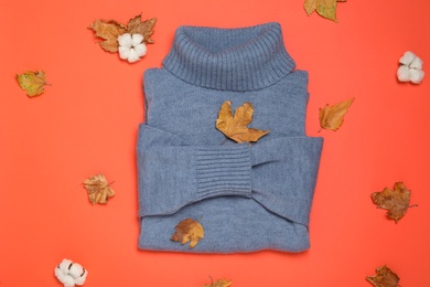 Warm sweater, dry leaves and cotton flowers on orange background, flat lay. Autumn season