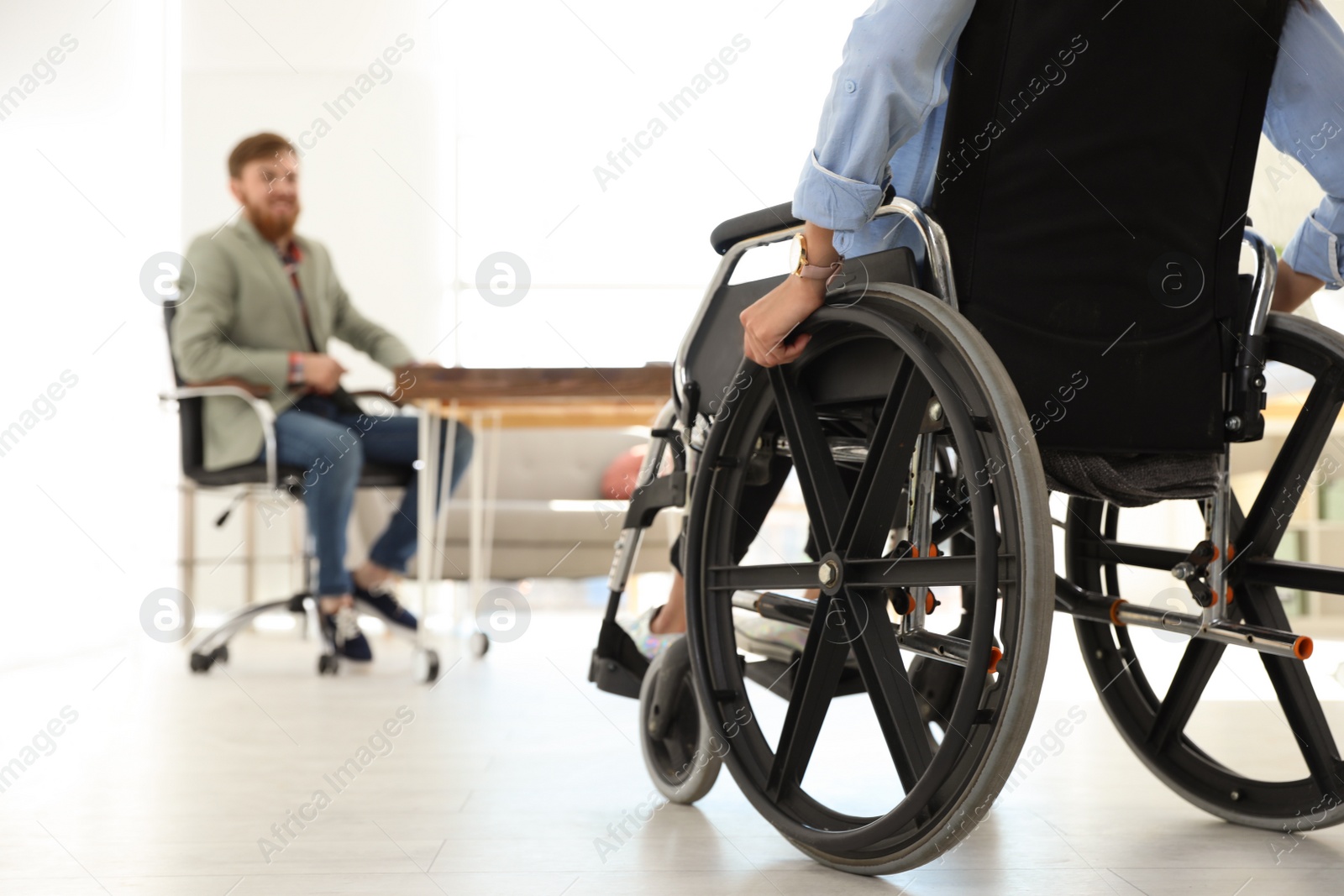 Photo of Young woman in wheelchair with colleague at office, closeup