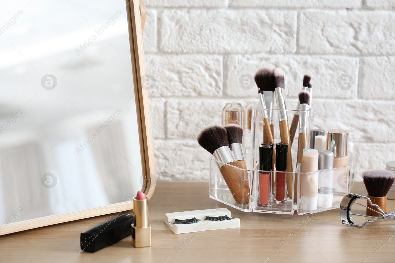 Photo of Organizer with cosmetic products for makeup on table near brick wall