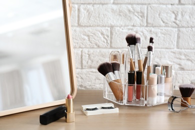 Organizer with cosmetic products for makeup on table near brick wall