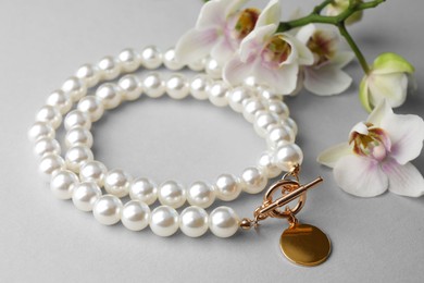 Elegant pearl necklace and orchid flowers on white background