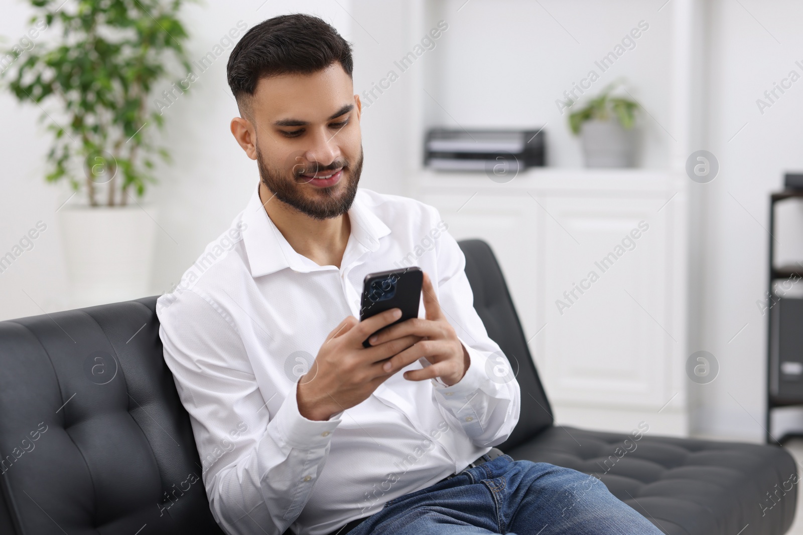 Photo of Handsome young man using smartphone on sofa in office