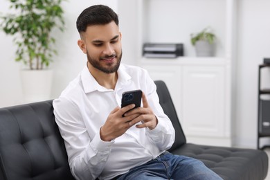 Handsome young man using smartphone on sofa in office