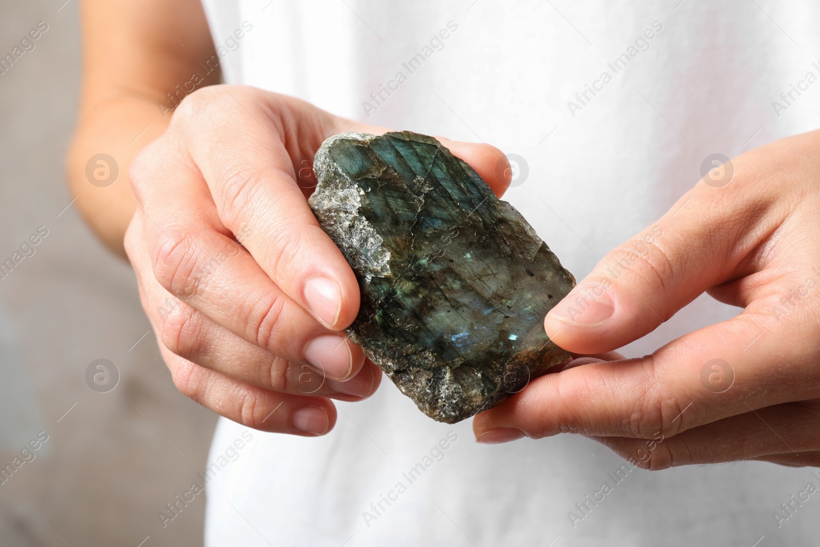 Photo of Young woman holding beautiful labradorite gemstone on beige background, closeup