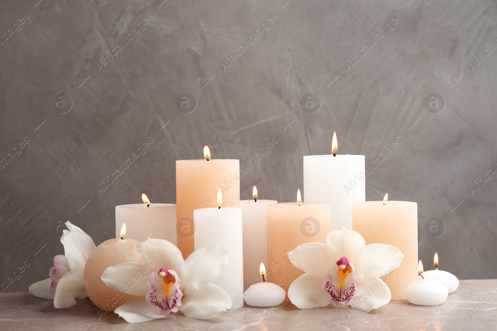 Photo of Beautiful composition with candles and flowers on table against grey background